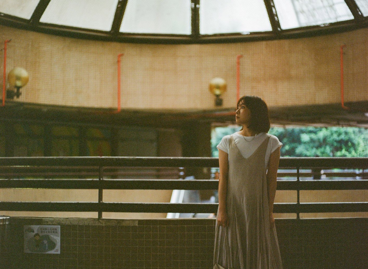 Portrait photography session at Hin Keng Estate—young woman in a flowy dress standing indoors under a domed skylight, with soft window light and public estate architecture in the background.