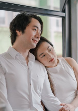 Romantic prewedding portrait of a young couple leaning together by the window at their alma mater in Hong Kong, both smiling in soft light, part of a seaside series (1/14).