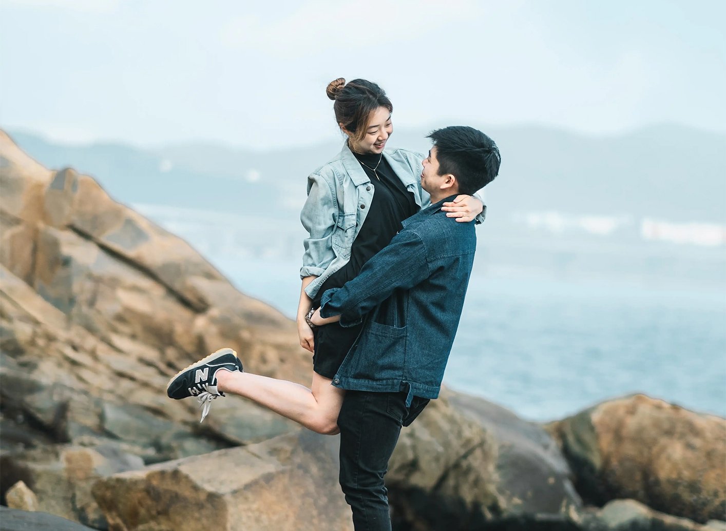 Playful couple embracing on rocks by the sea during Lei Yue Mun Hong Kong engagement photoshoot