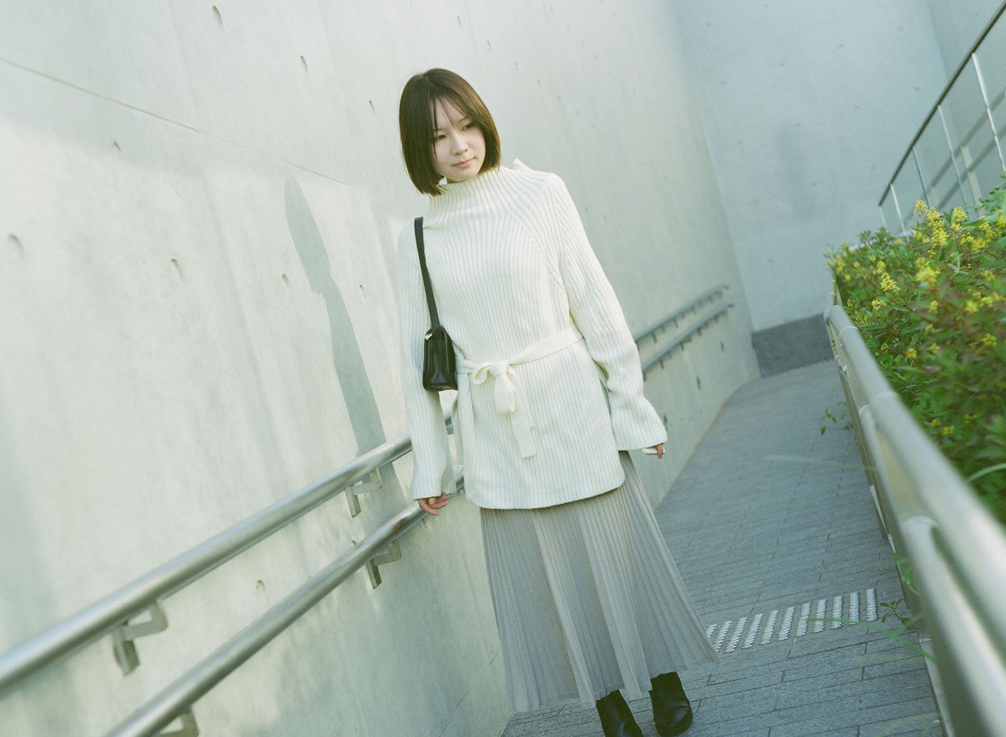 Portrait of a young woman in a white sweater and pleated skirt on a minimalist concrete ramp at WKCD, West Kowloon Cultural District, Hong Kong.